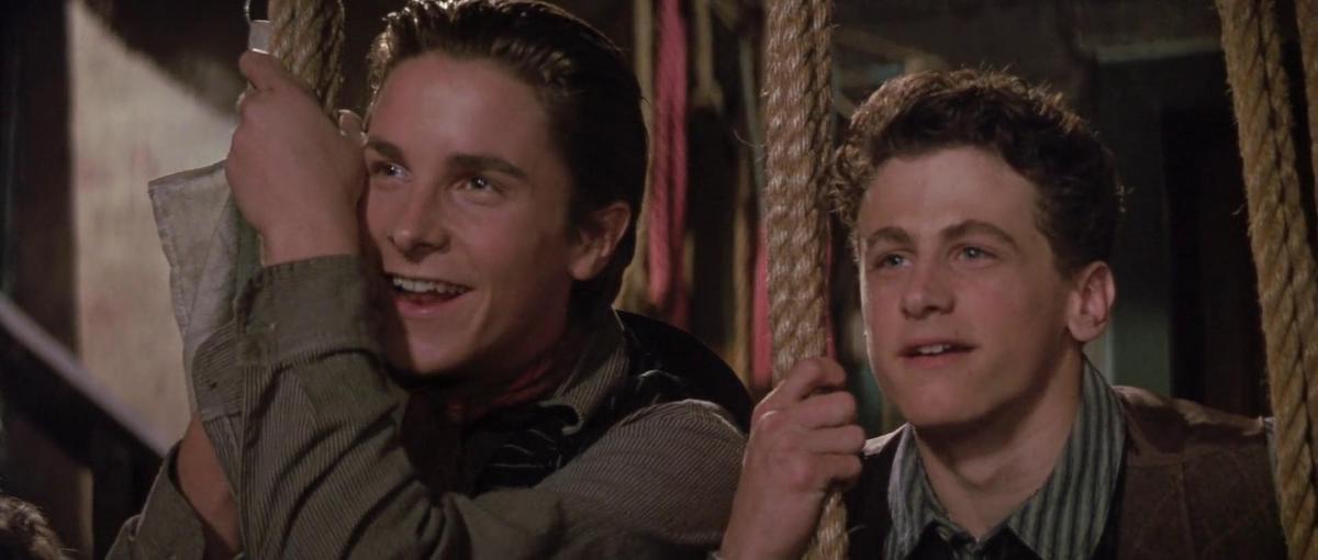 Christian Bale and David Moscow smile holding ropes and look on in the Disney movie ‘Newsies’
