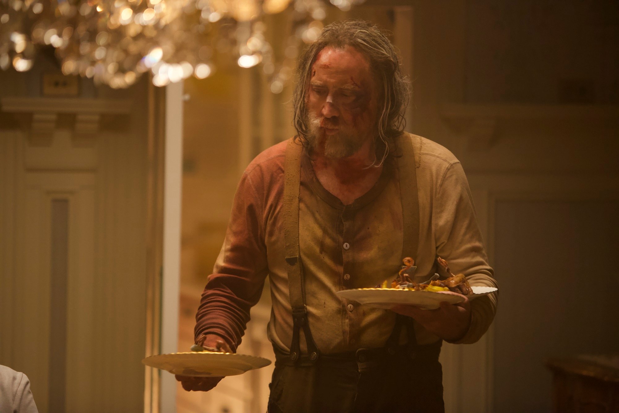 Nicolas Cage, bloodied after a fight, holds dinner plates