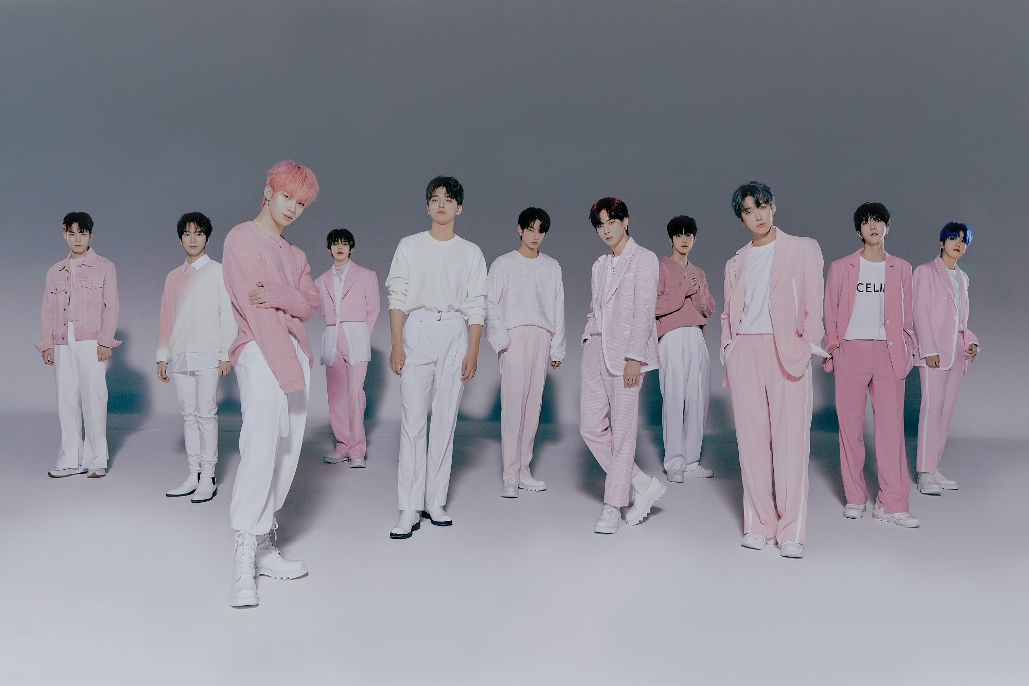 The members of K-pop group Omega X stand in a gray room wearing pink clothes for a promotional photo