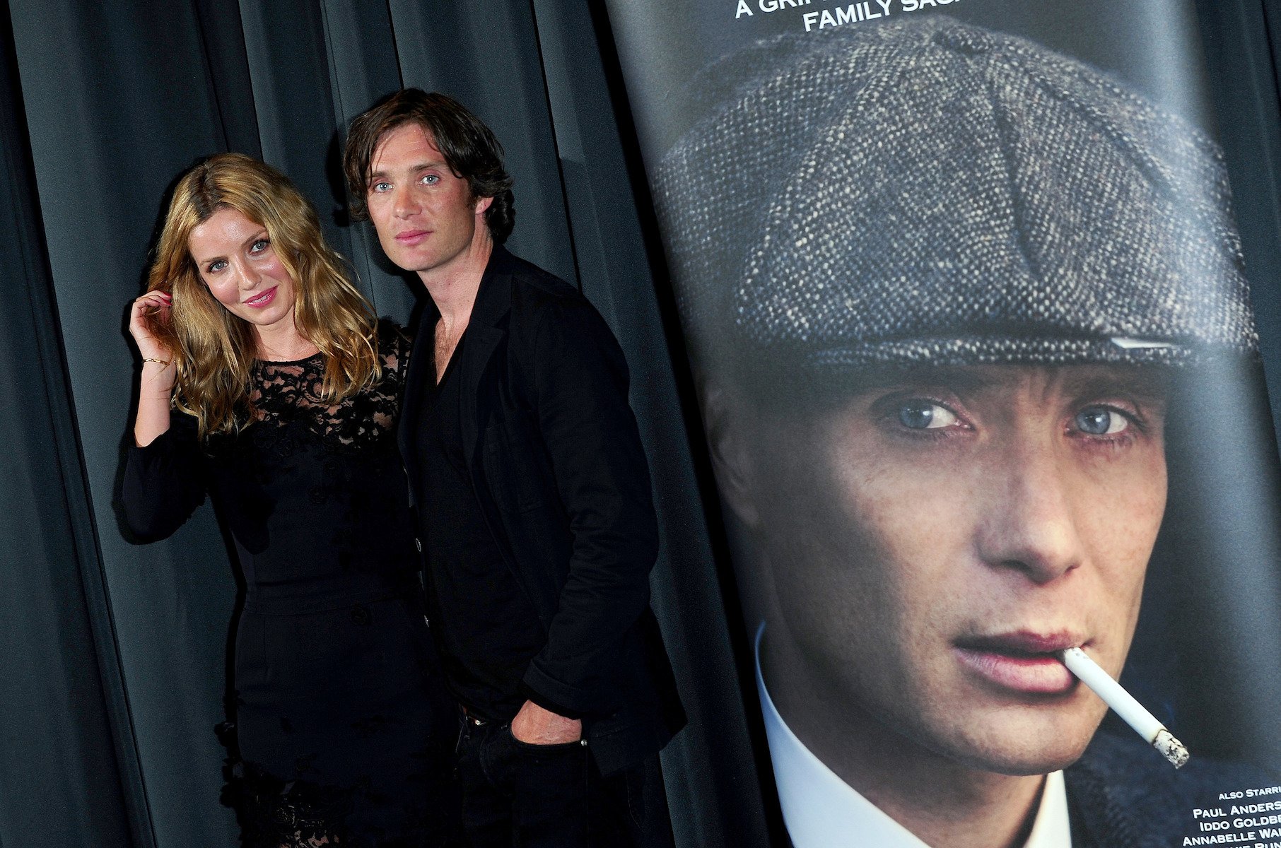 Annabelle Wallis and Cillian Murphy from 'Peaky Blinders' Season 6 standing next to each other and a poster of Thomas Shelby
