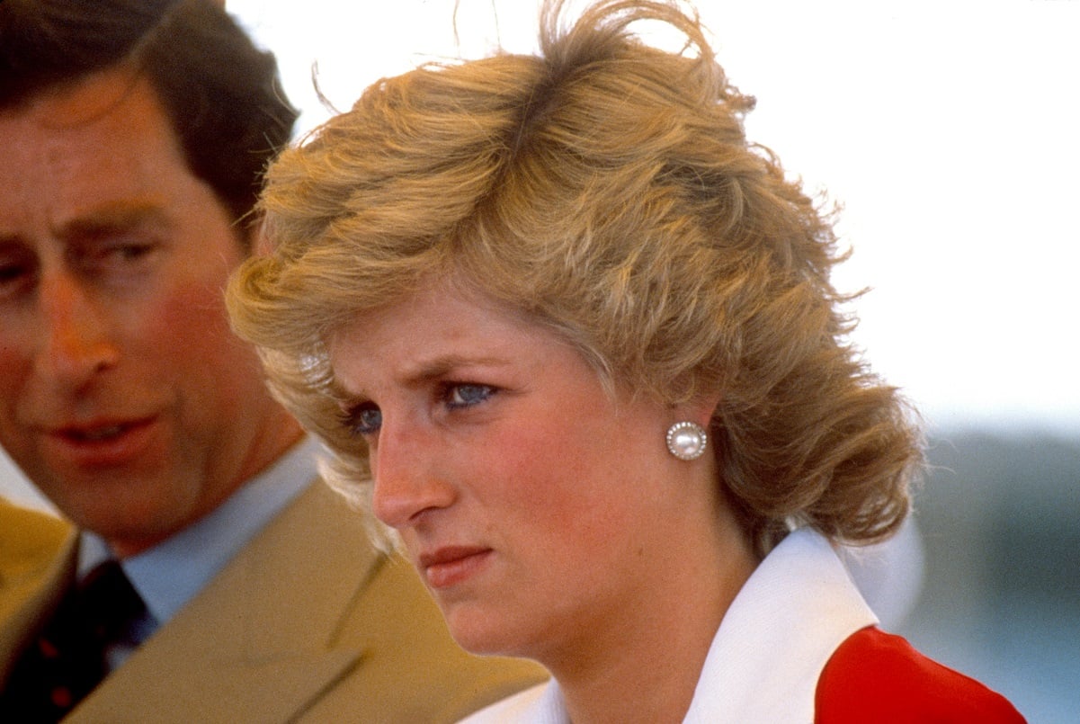 Princess Diana pictured from just below her neck up standing near Prince Charles in a red dress with a white collar