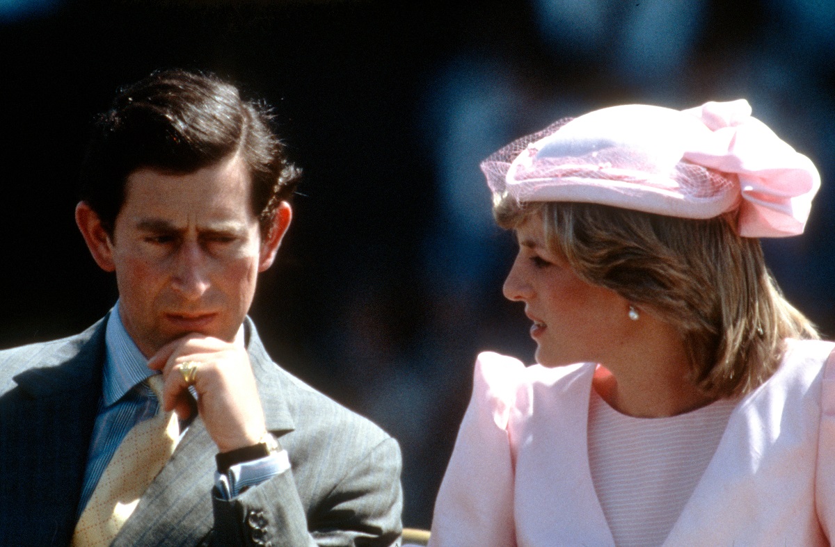 Princess Diana wearing a pink dress and fascinator while seated next to Prince Charles who looks to be in deep thought