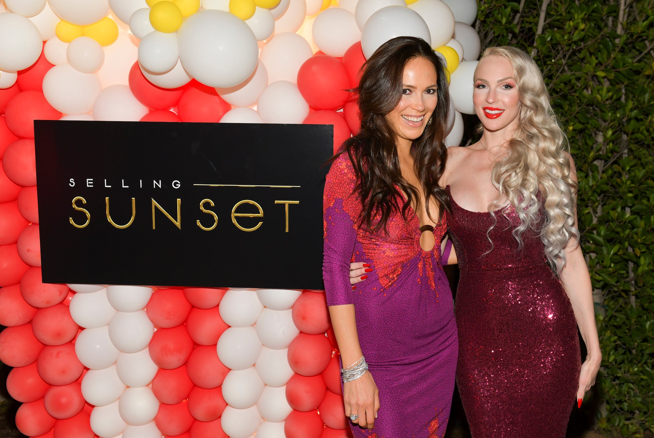 Davina Potratz (L) and Christine Quinn from 'Selling Sunset' Season 4 standing with their arms around each other next to a 'Selling Sunset' sign at a viewing party