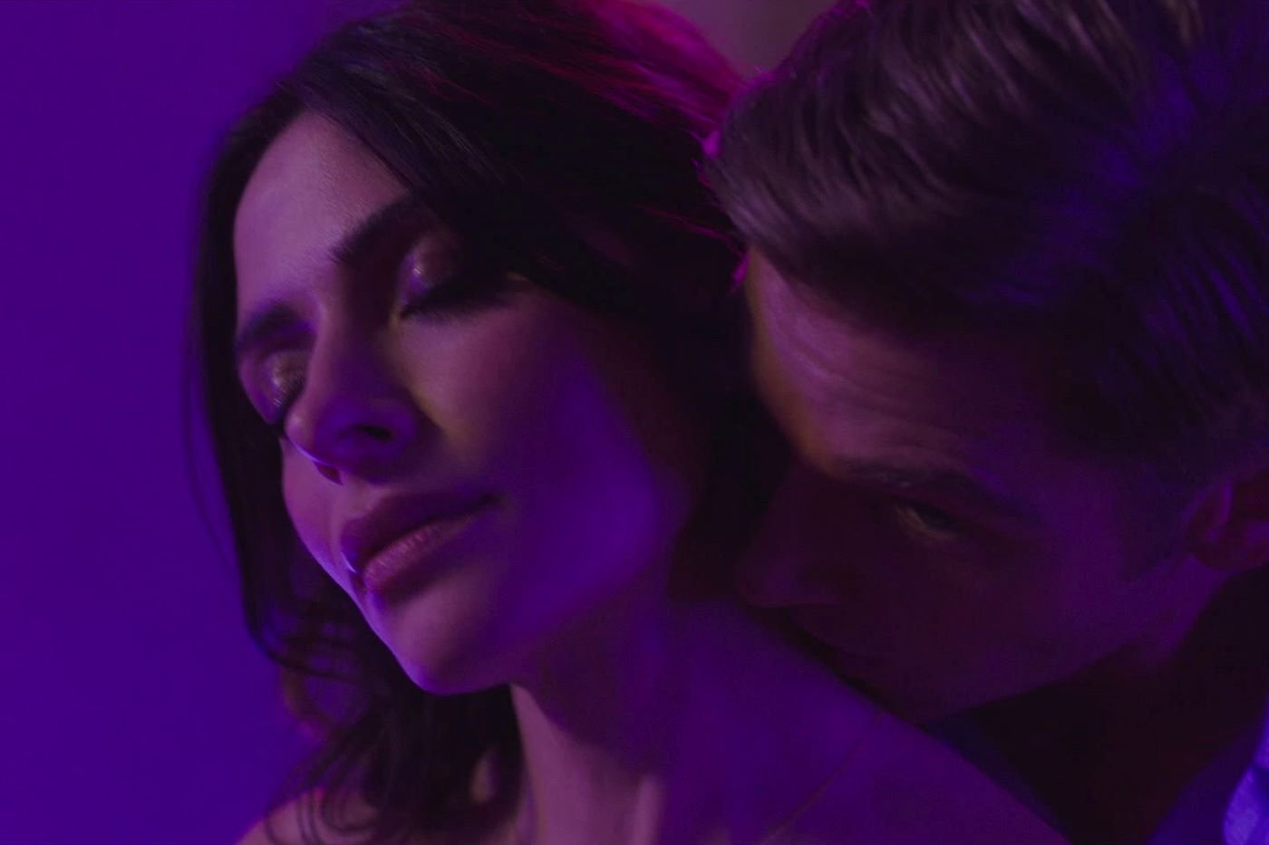 A scene from Sex/Life with Adam Demos kissing Sarah Shahi's neck.