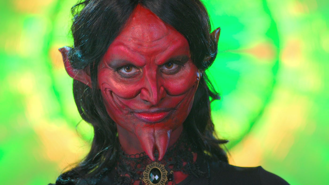 A person dressed up as a devil in the Netflix series 'Sexy Beasts' with black hair and green background.