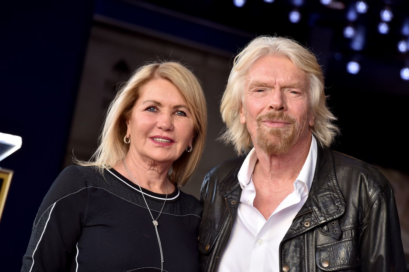 Picture of Joan Templeman, dressed in a black and grey top, and Sir Richard Branson, dressed in a white button-up shirt and black leather jacket in front of a blacked out background with a few blue lights scattered in the right-hand corner.
