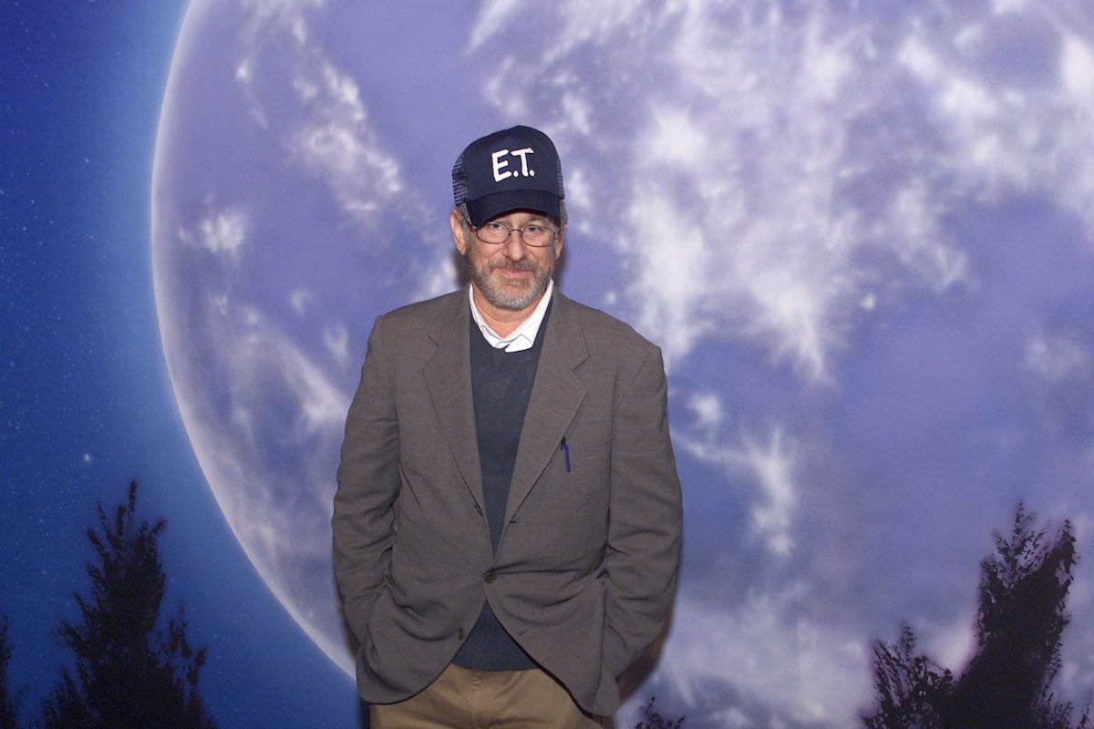 Steven Spielberg wears an ‘E.T’ hat and poses in front of the movie’s poster