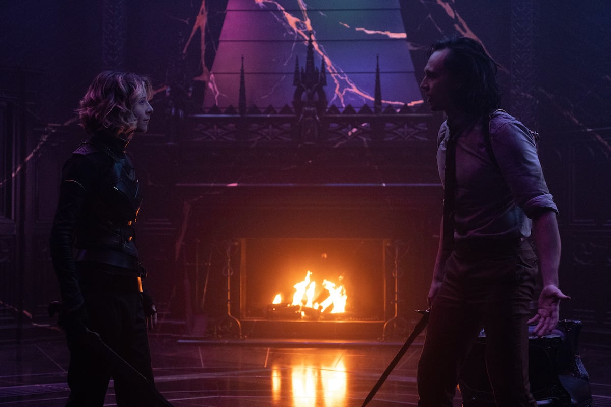 Sophia Di Martino as Sylvie and Tom Hiddleston as Loki in 'Loki' Season 1 Episode 6. They stand across from each other armed with blades. The room is dark and purple and there's a fire burning in the fireplace in the background.