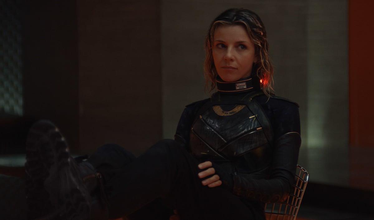 Sophia Di Martino in 'Loki' Episode 4. She wears a black and green armored body suit with an electronic band around her neck. Her hair is wet and she has her feet up on a table.