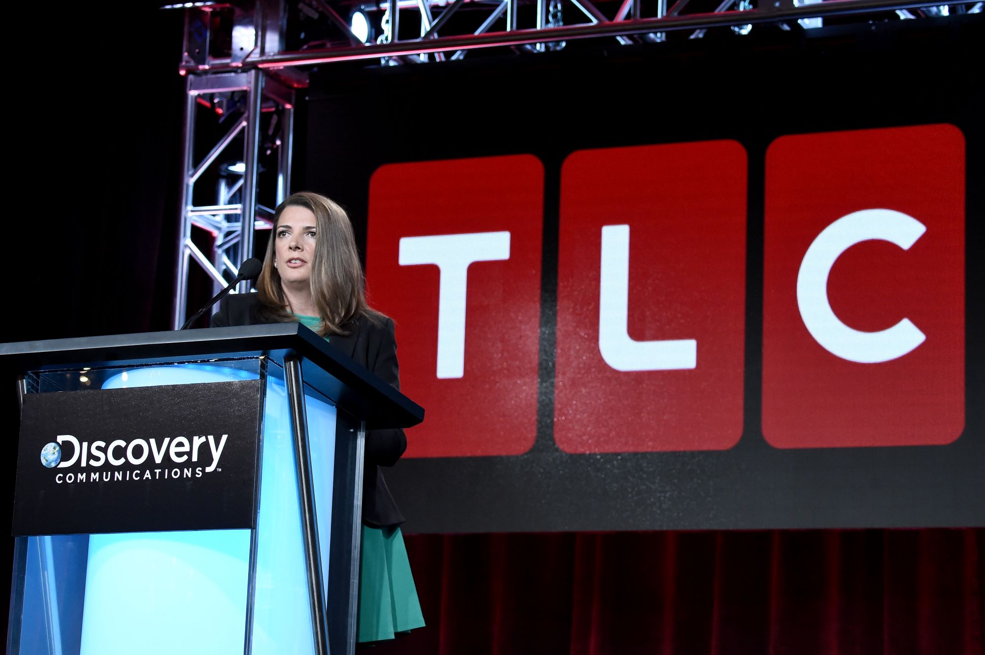 TLC General Manager Nancy Daniels standing in front of a TLC sign speaking at a podium.