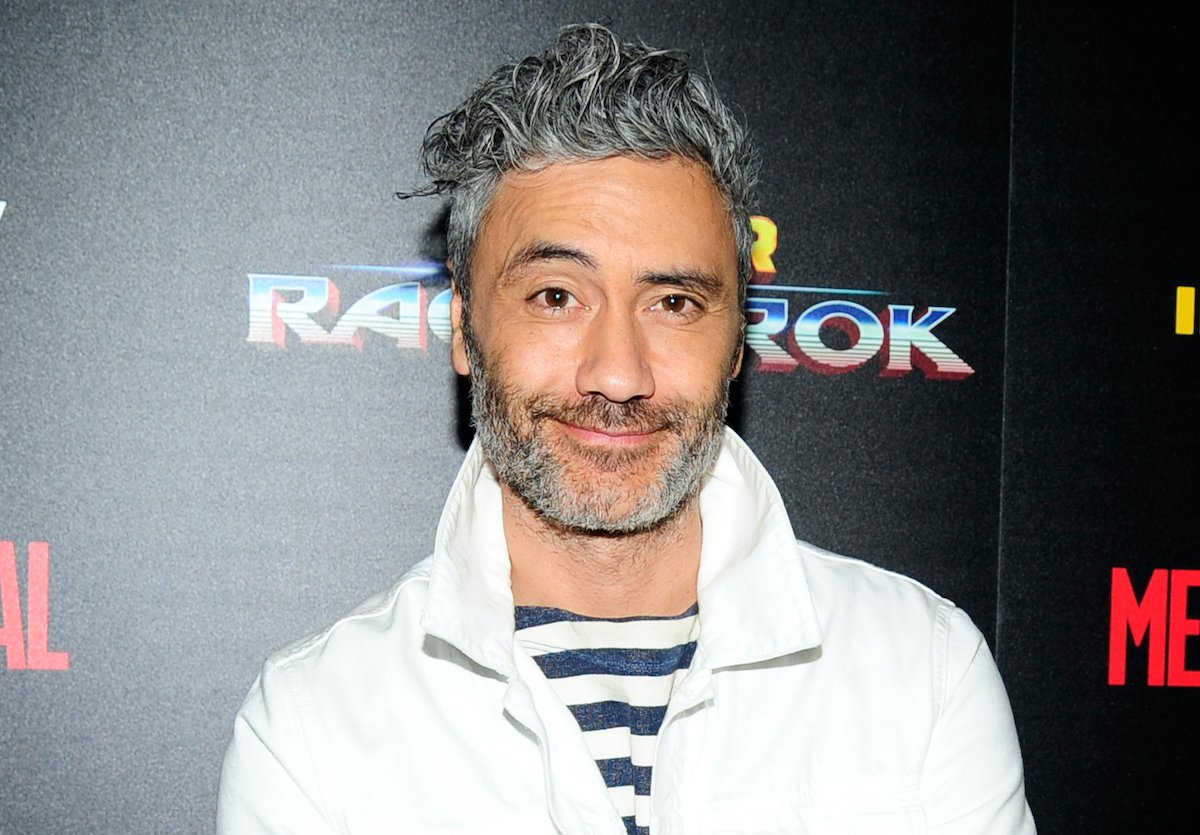 'Thor: Ragnarok' and 'Thor: Love and Thunder' director Taika Waititi smiles in front of a black backdrop that says 'Thor: Ragnarok'