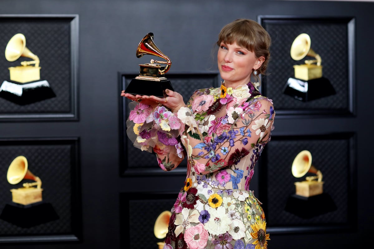 Taylor Swift holds her Grammy for 'folklore' while wearing a flower dress and her signature red lip
