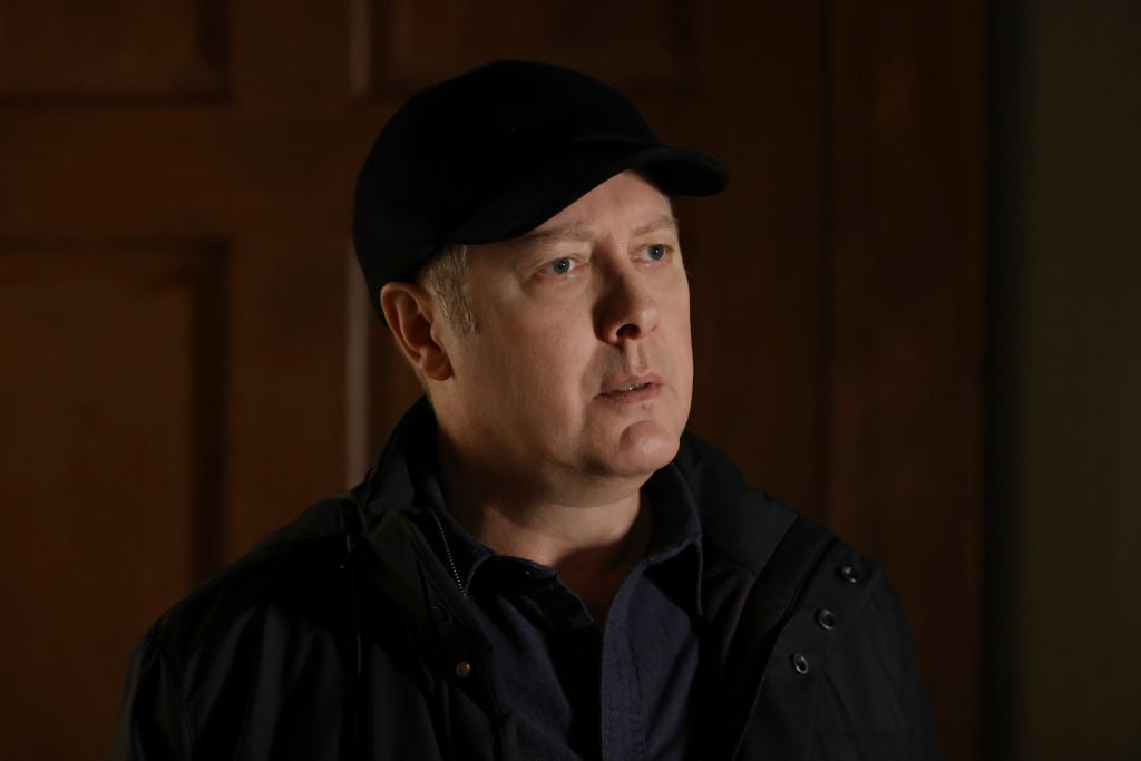 James Spader as Raymond 'Red' Reddington looks concerned. He's wearing a dark jacket and baseball cap.