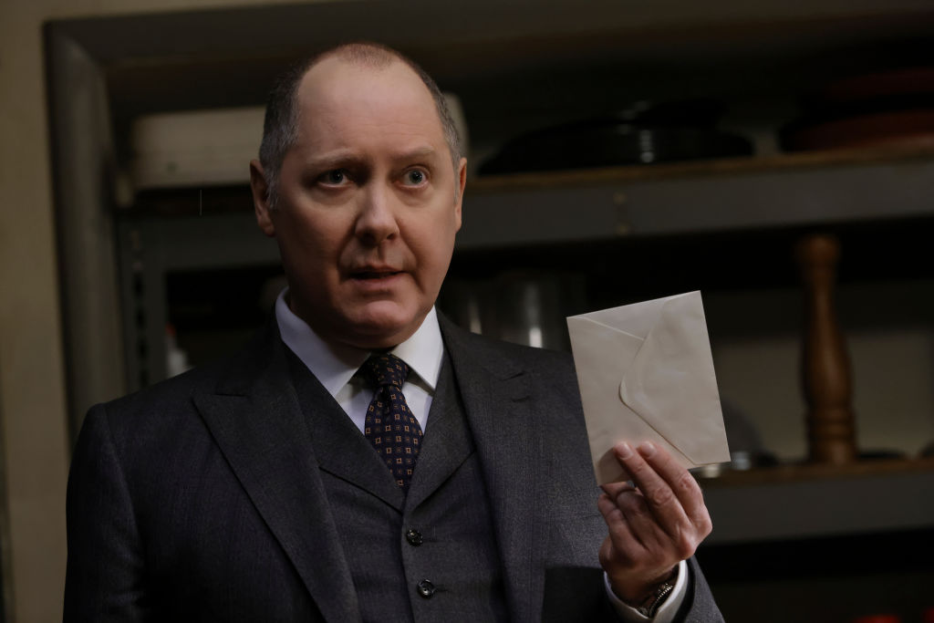 James Spader as Raymond 'Red' Reddington is dressed in a suit and tie. He holds an unopened letter.