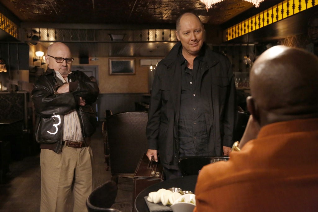 Clark Middleton as Glen Carter and James Spader as Raymond 'Red' Reddington stand in front of a man on the phone. 