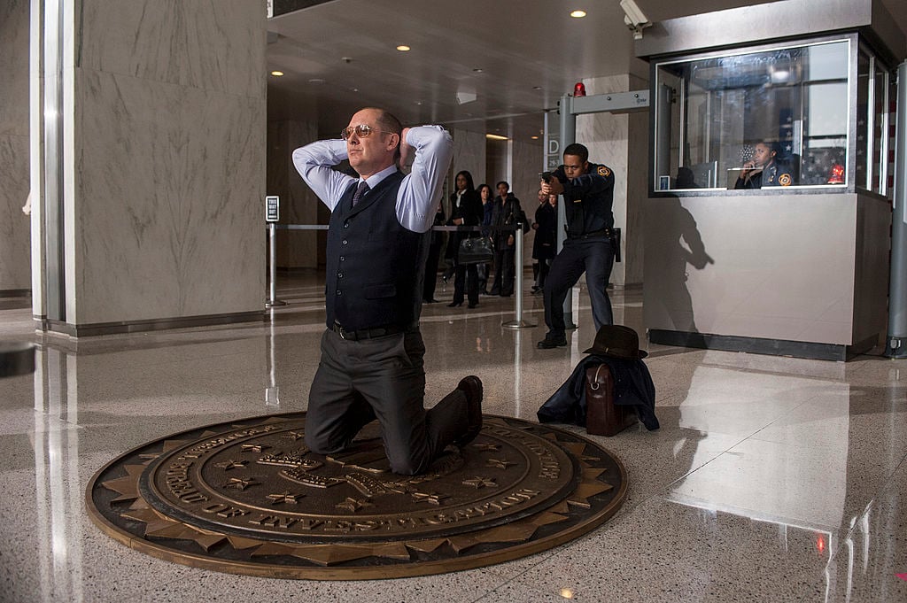 James Spader as Raymond 'Red' Reddington turns himself into the FBI. He's kneeling with his hands behind his head.