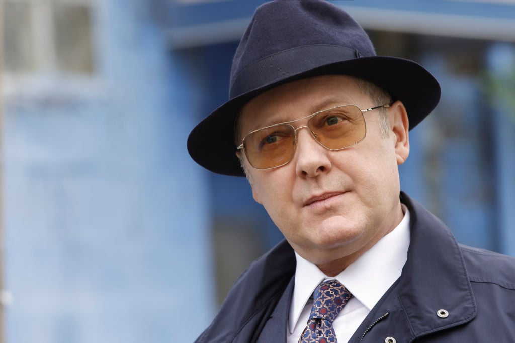 James Spader as Raymond 'Red' Reddington looks on in his trademark fedora and sunglasses.