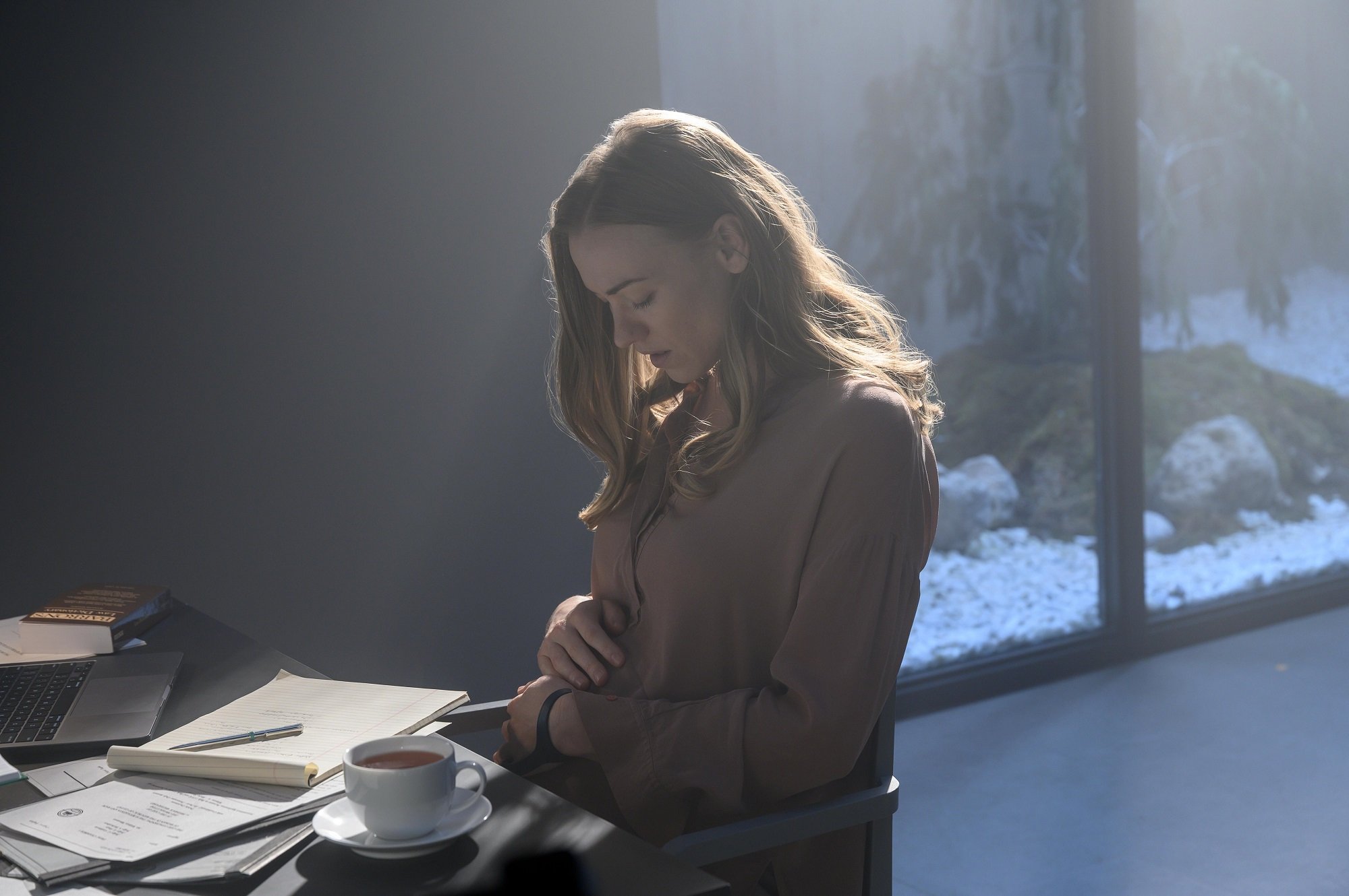 Serena Joy Waterford cradles her pregnant stomach while sitting at a desk in 'The Handmaid's Tale'