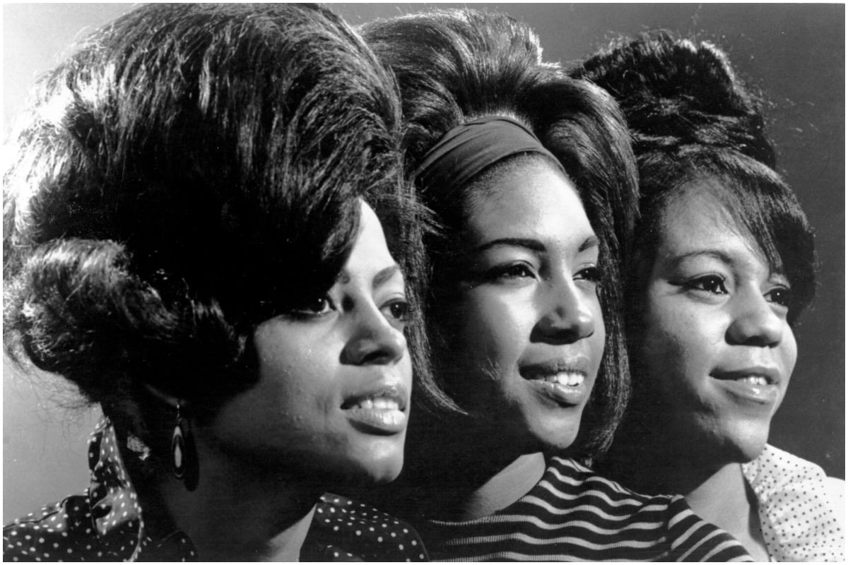 The Supremes: Diana Ross, Mary Wilson, and Florence Ballard smiling in a black and white photo.