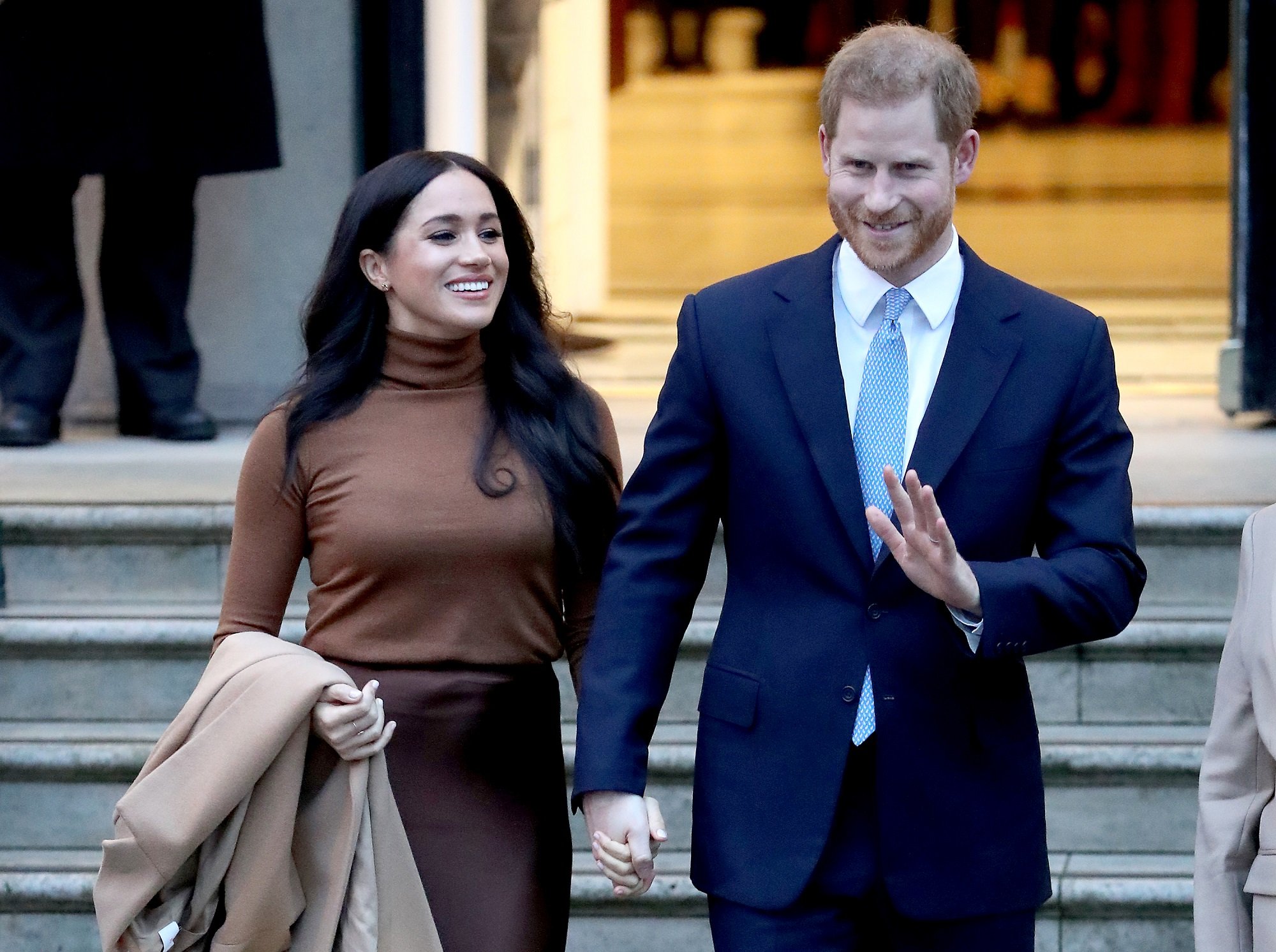 Meghan Markle wears a brown outfit holding hands with Prince Harry in a suit