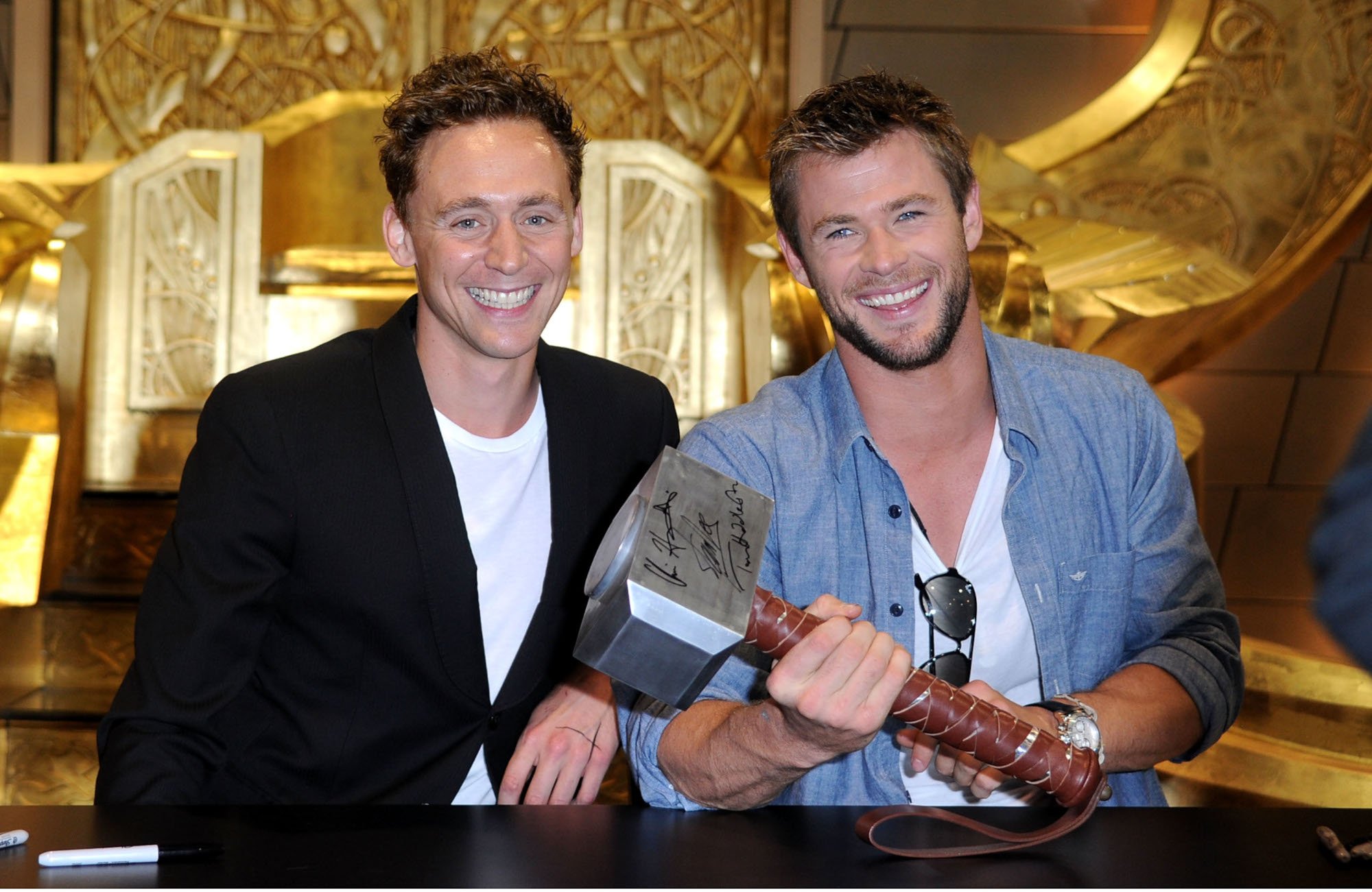'Loki' star Tom Hiddleston sits next to Chris Hemsworth, who is holding Thor's hammer