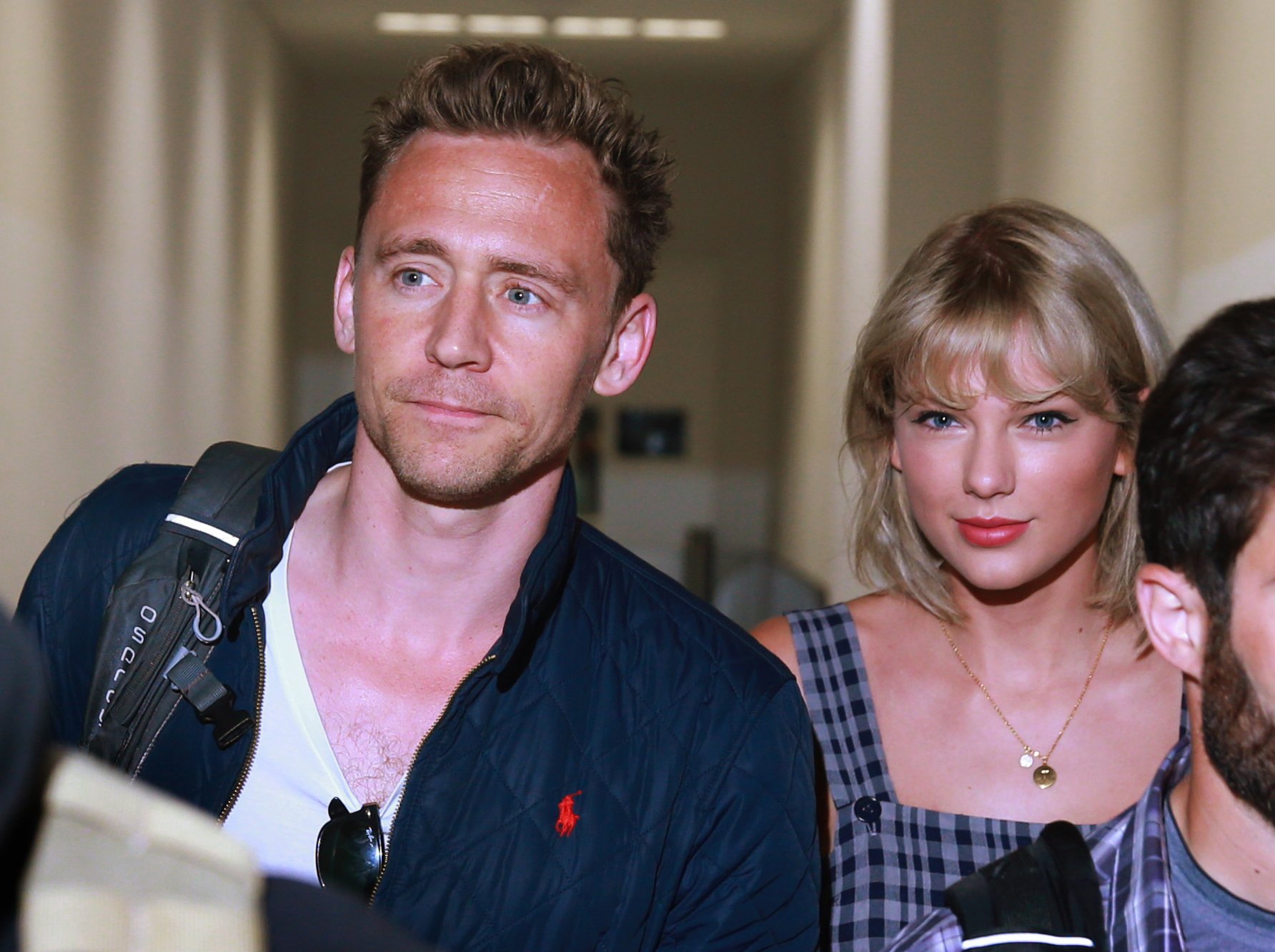 Tom Hiddleston wearing a white shirt and blue jacket and standing next to Taylor Swift