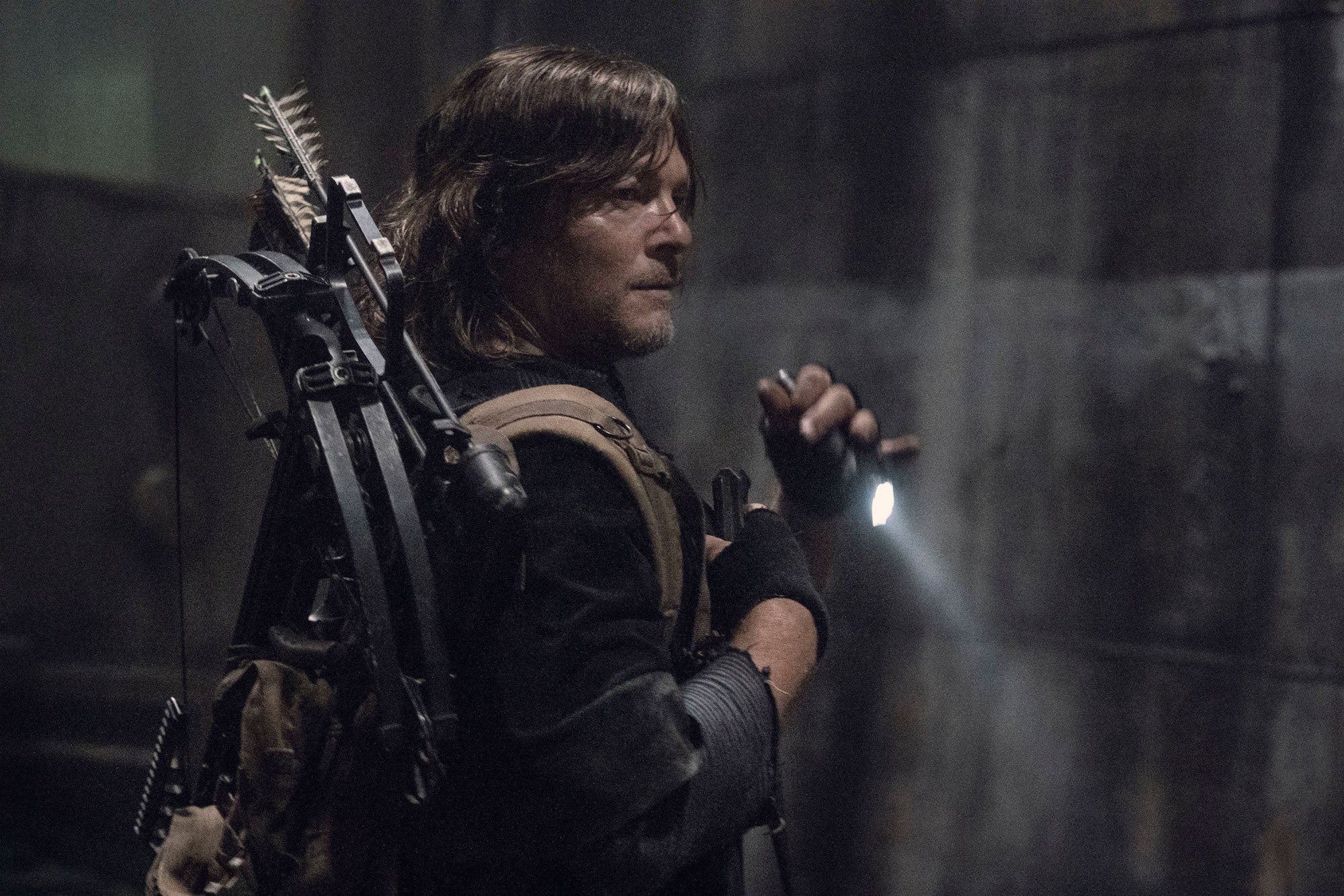 Norman Reedus in the final season of 'The Walking Dead' is standing in the dark, holding a knife, and looking over his shoulder