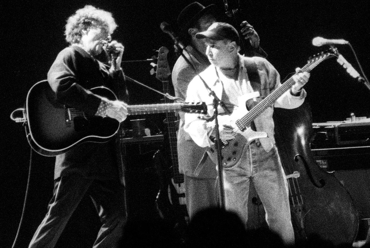 Bob Dylan plays harmonica and looks at Paul Simon, who plays guitar to his left at a '99 concert.