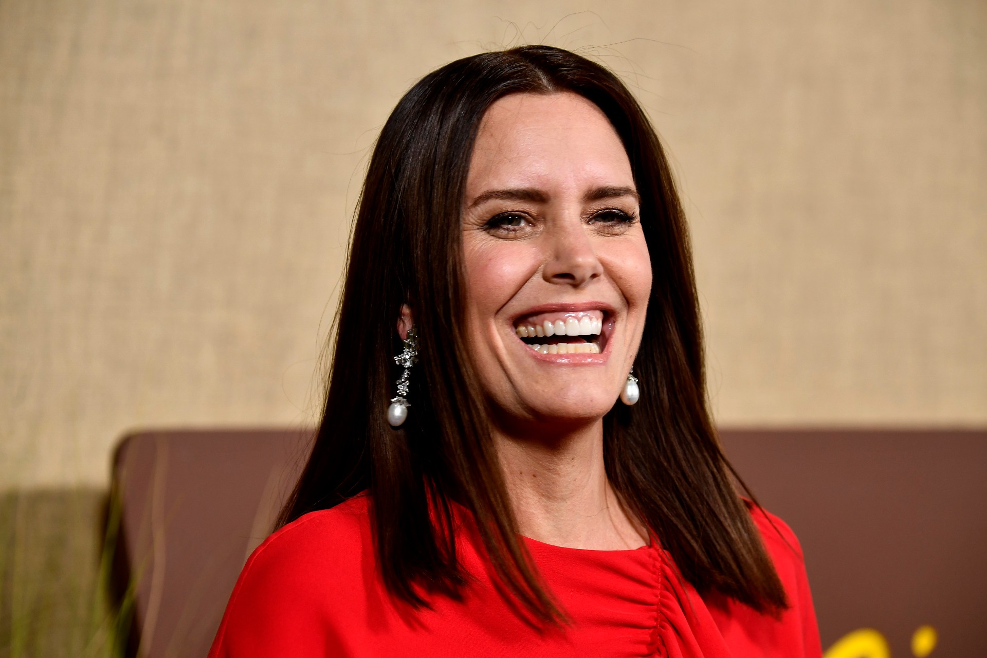 ione skye smiles while wearing a red outfit