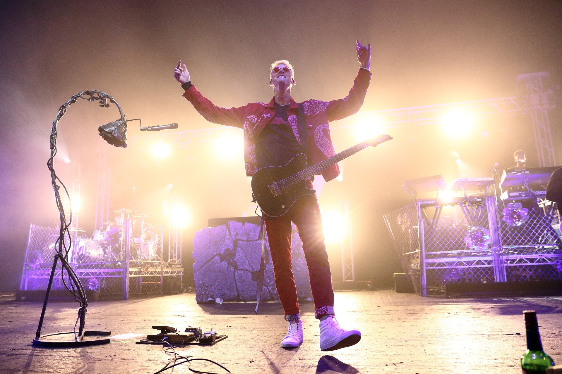 Machine Gun Kelly raises his hands during a performance while wearing a guitar.