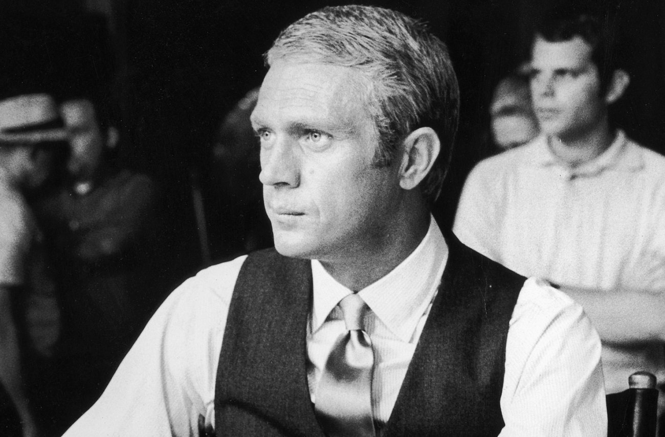 Steve McQueen, wearing a tie and vest, sits in a chair on the set of 'The Thomas Crown Affair.'