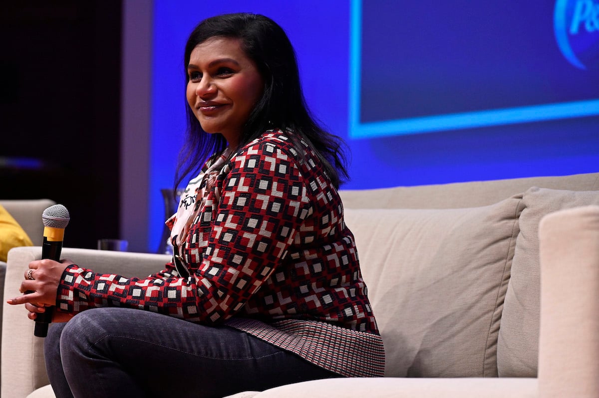 Mindy Kaling sitting on a couch and holding a microphone
