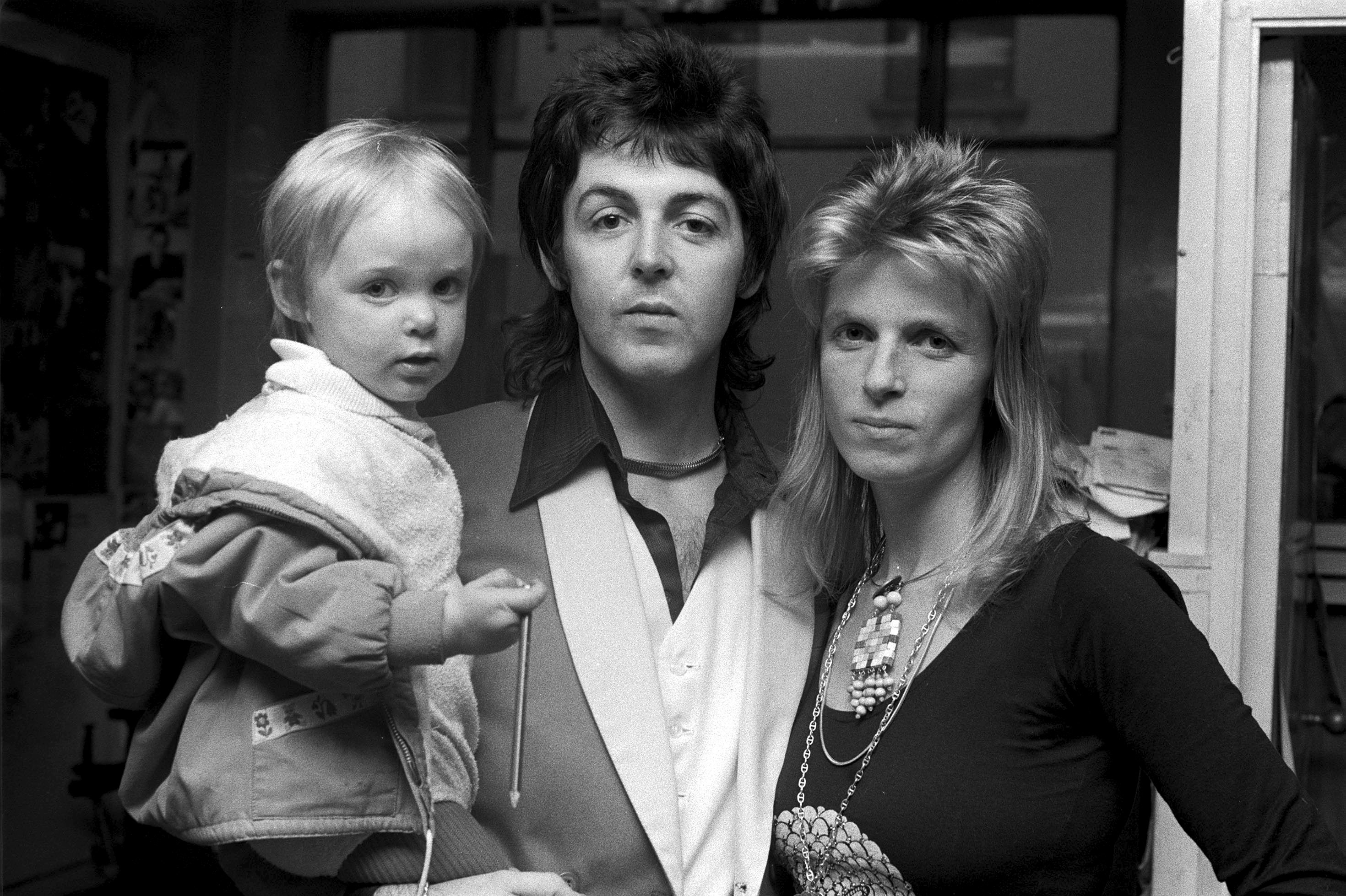 Paul McCartney holding baby Stella McCartney while Linda McCartney stands to his right