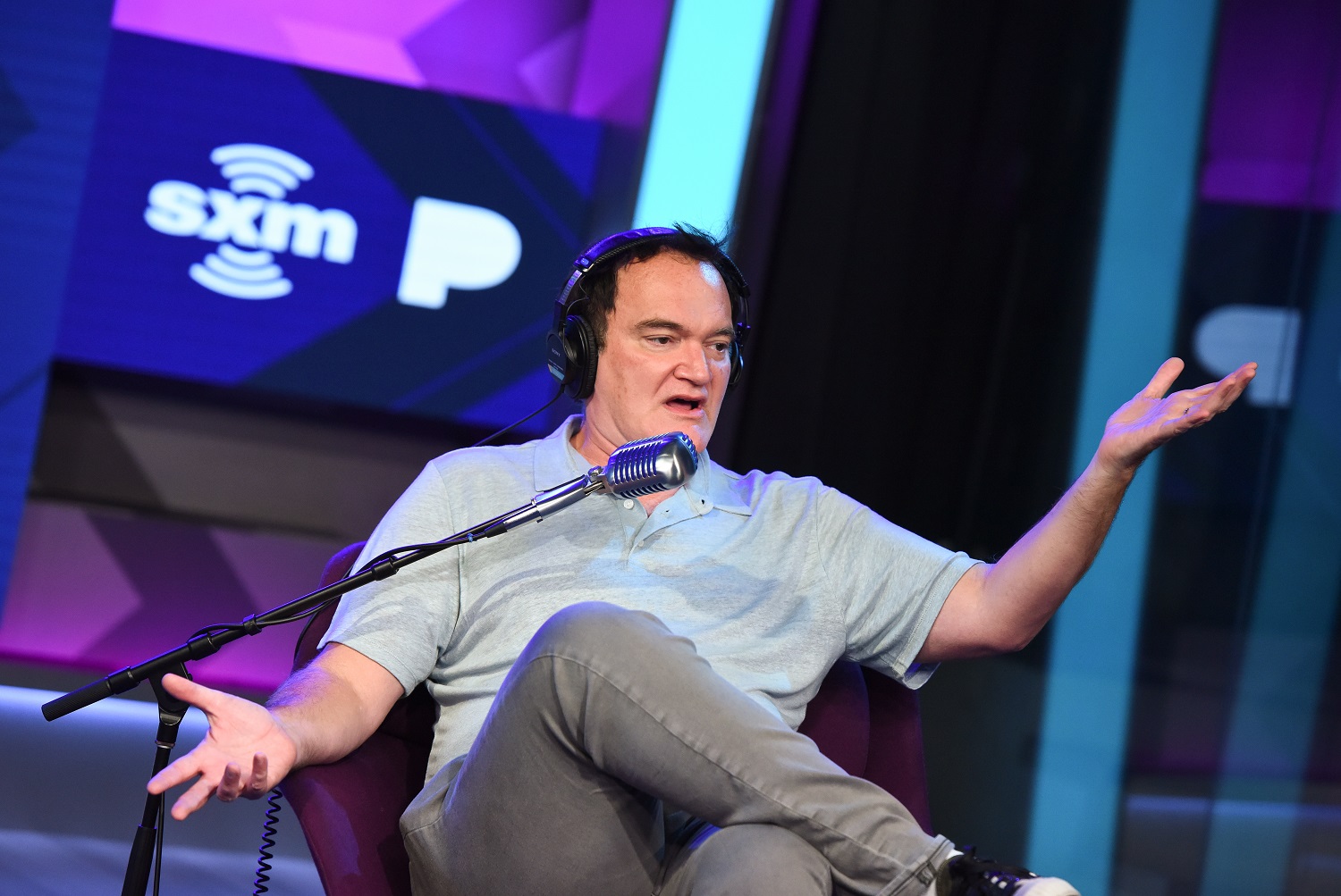 Quentin Tarantino sits in a chair and speaks into a microphone during an interview.