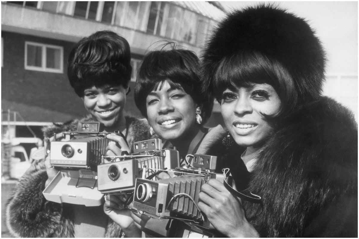 Diana Ross and the Supremes smiling and holding cameras in London.