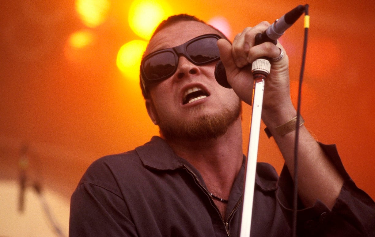 Scott Weiland sings into the microphone wearing sunglasses.