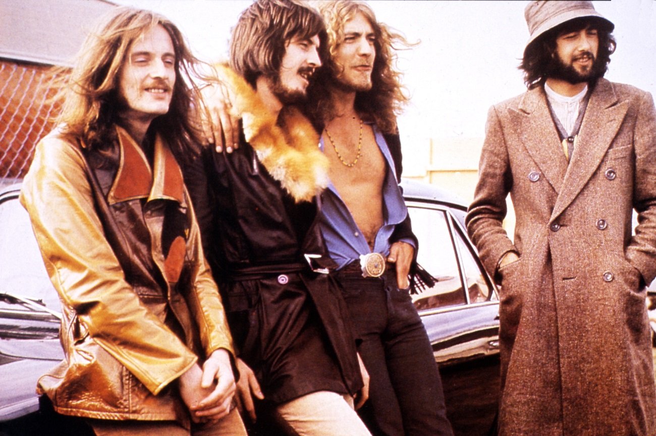 Group photo of Led Zeppelin, circa 1970, with the band members leaning against a car and looking off-camera