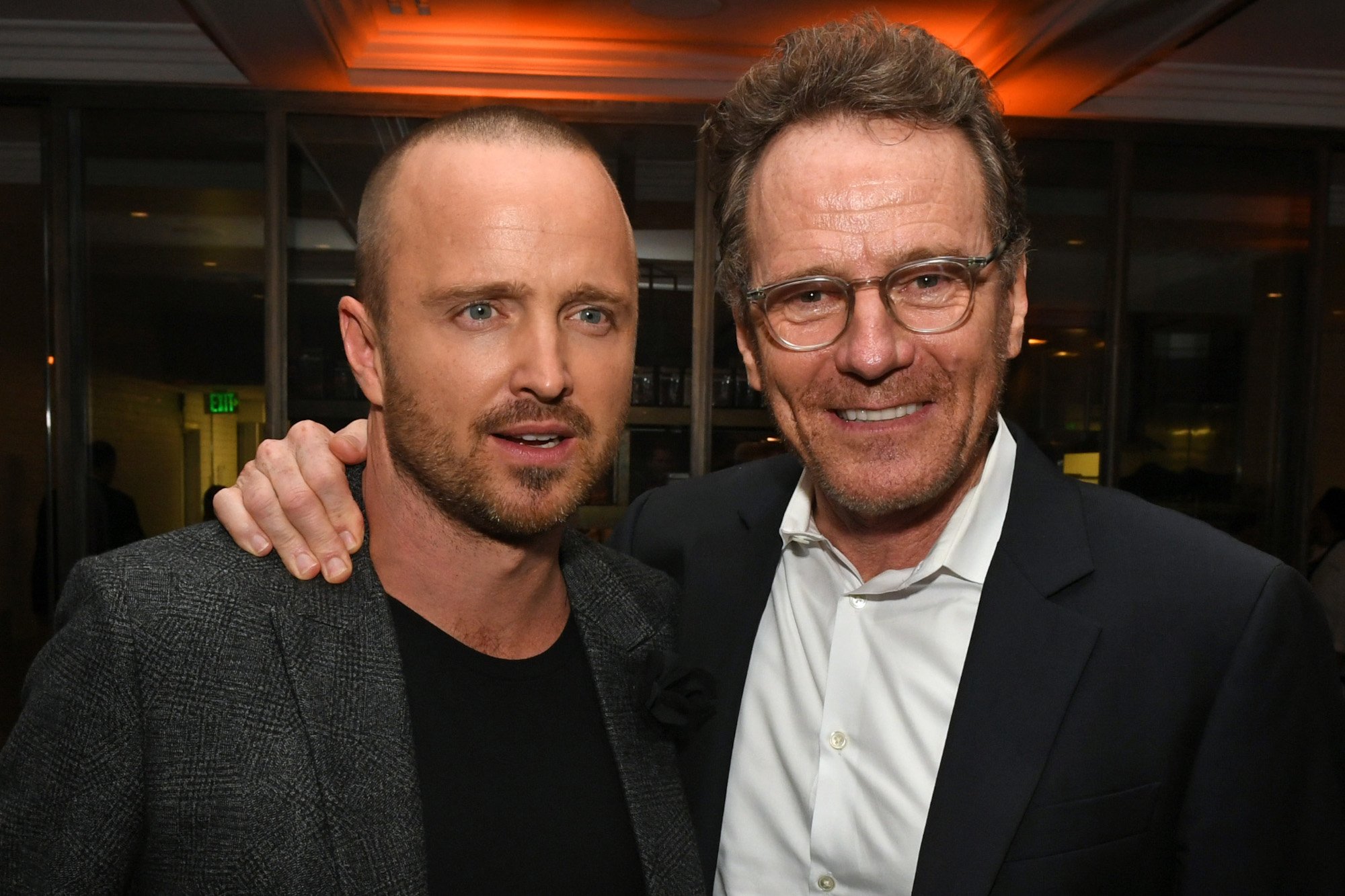 Walter White star Bryan Cranston on the left with his arm around 'Breaking Bad' co-star Aaron Paul. They're both wearing suits, and Aaron is looking to the left.