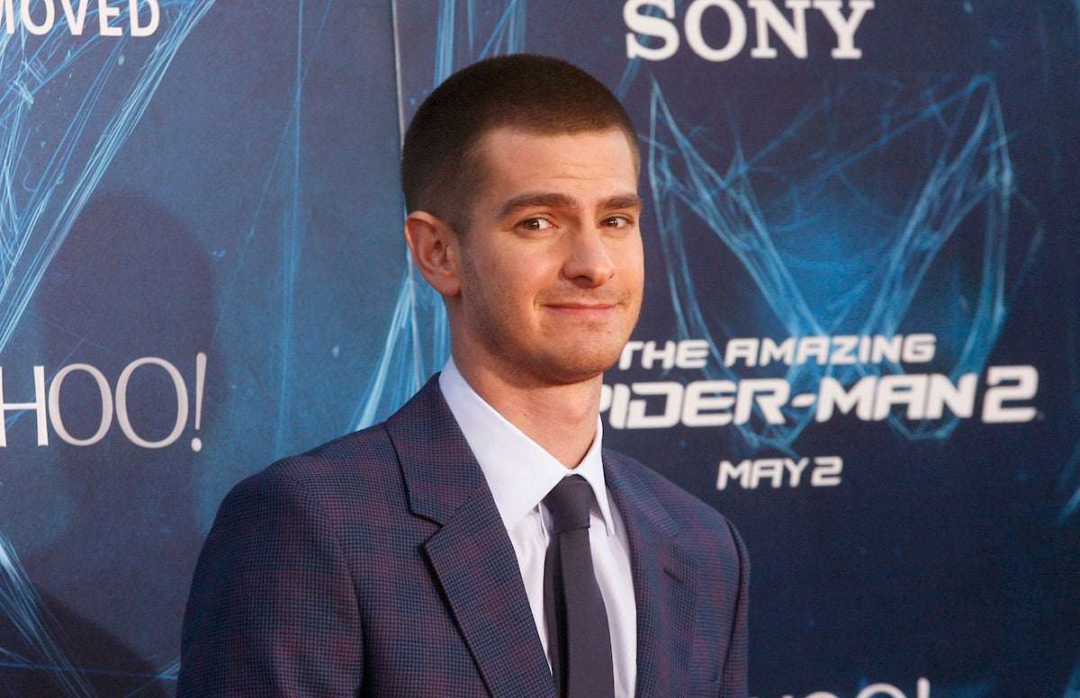 Andrew Garfield poses in a suit in front of ‘The Amazing Spider-Man 2’ logo