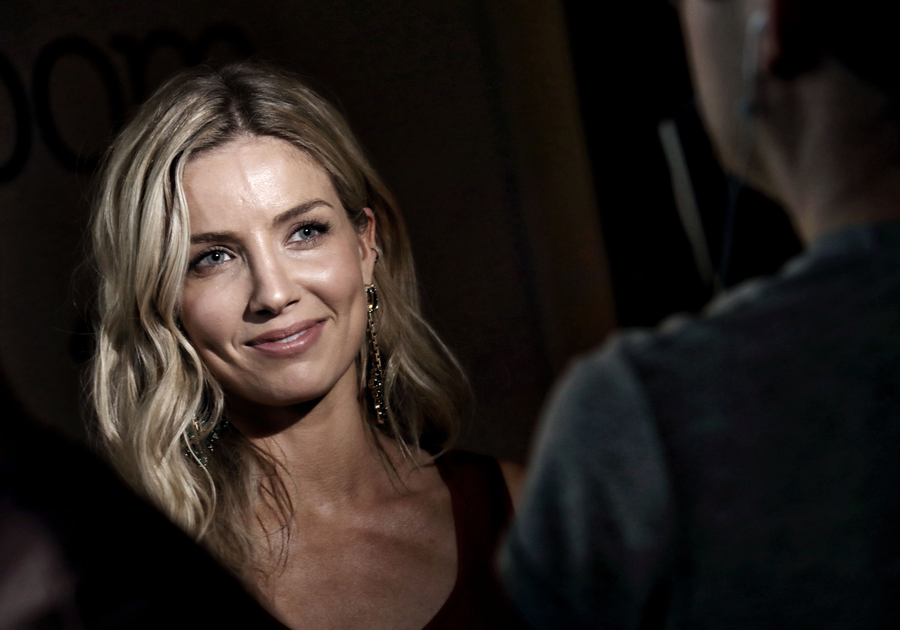 Annabelle Wallis smiles for a close up photo wearing long earrings.