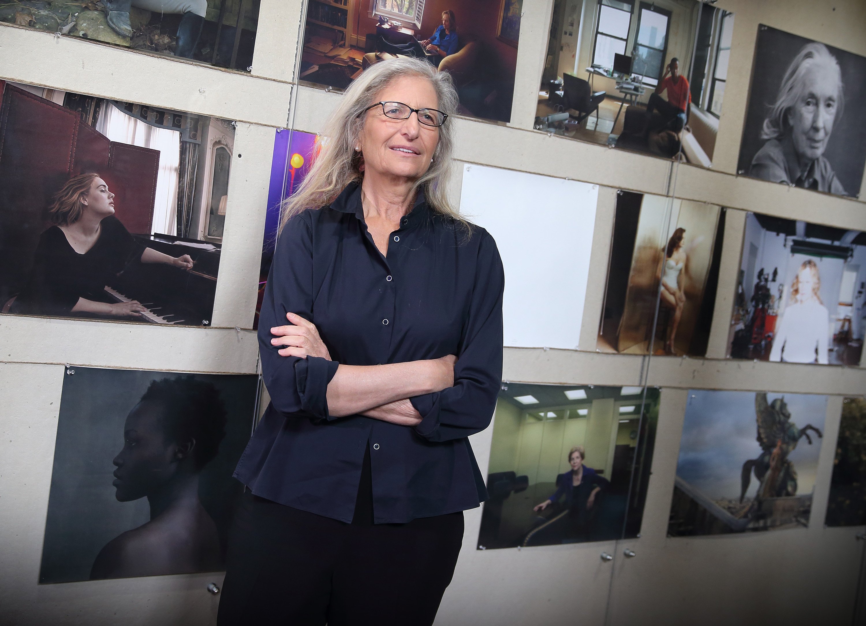 Annie Leibovitz in front of a wall with many pictures on it