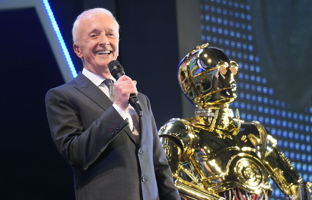 Anthony Daniels holds a microphone on stage next to C-3PO