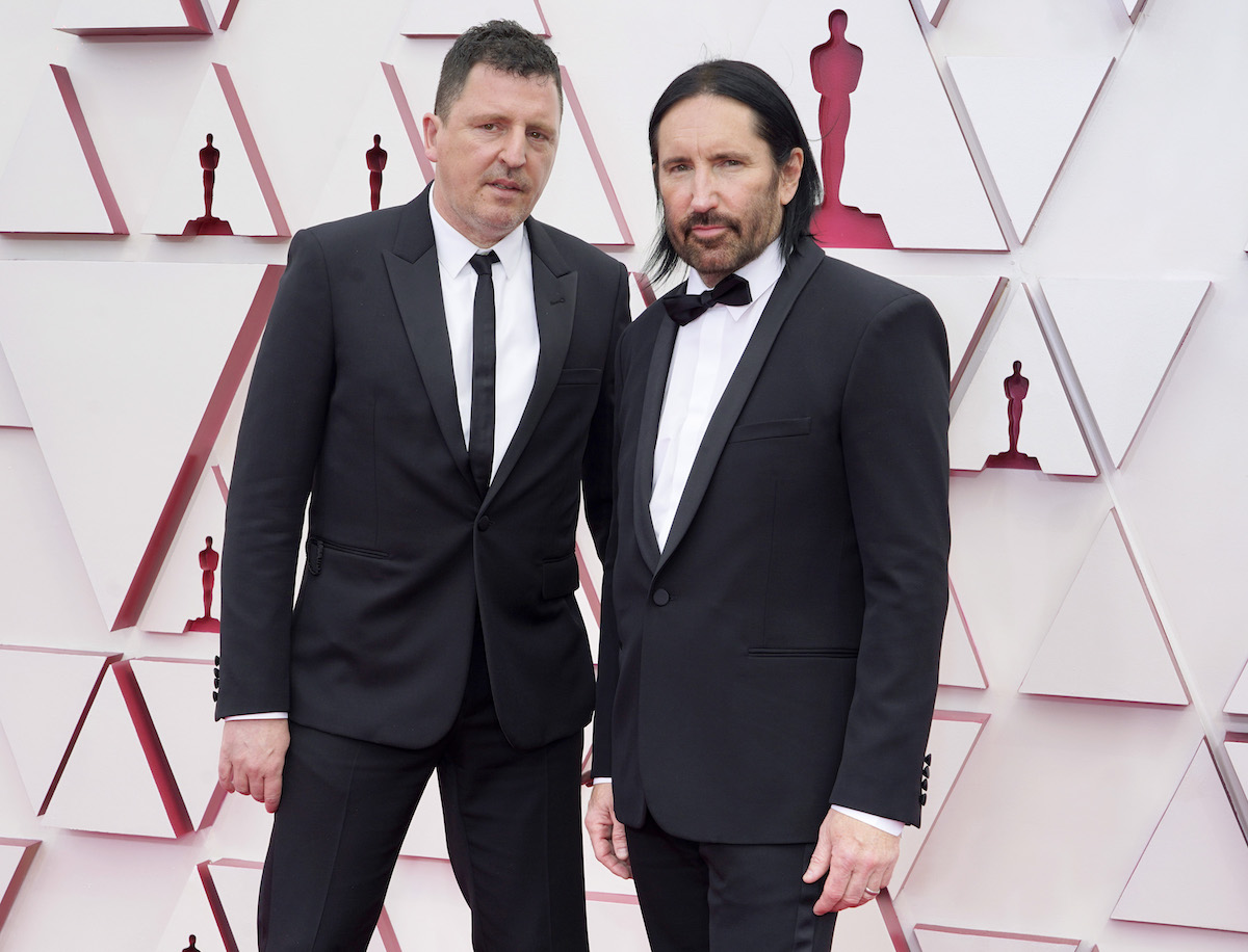 Atticus Ross and Trent Reznor wearing suits pose for the camera at an event.
