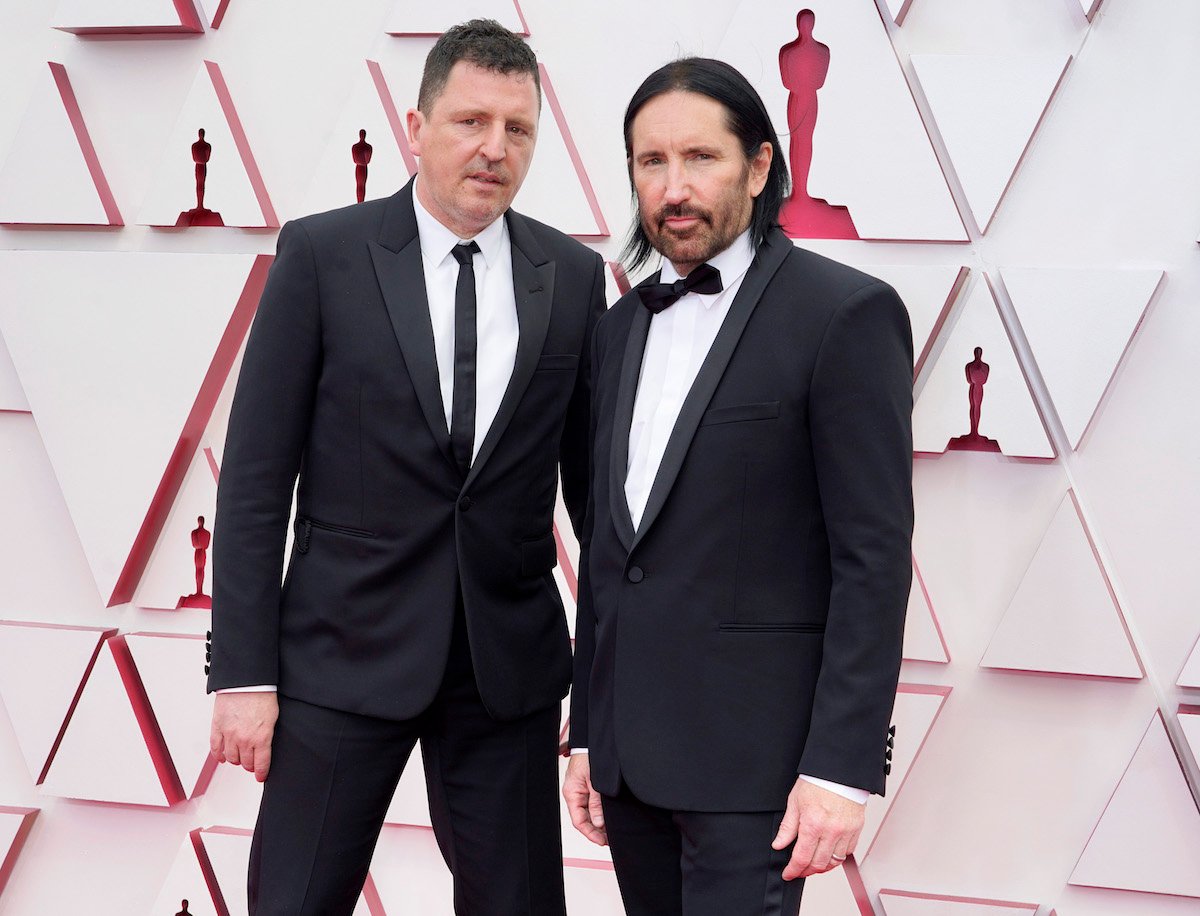 Atticus Ross and Trent Reznor wearing suits pose for the camera at an event.