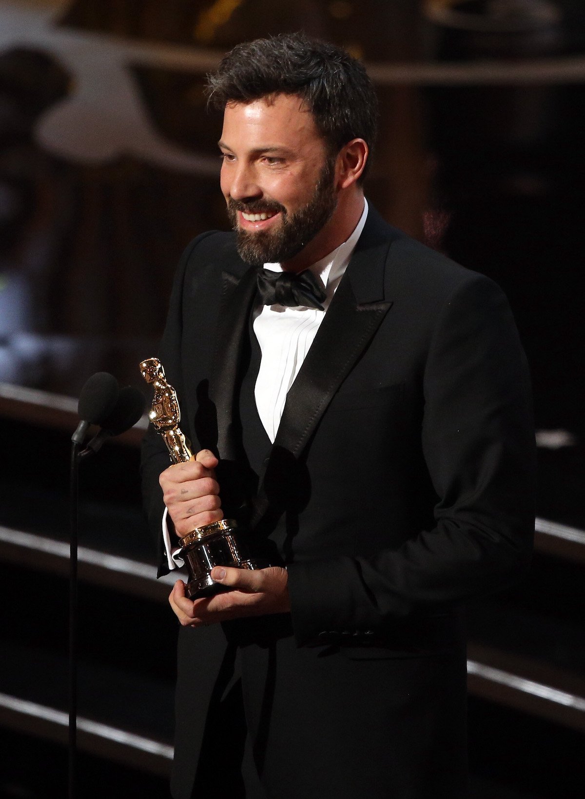 Ben Affleck smiles as he holds his Oscar onstage at the 2013 Academy Awards in a tuxedo