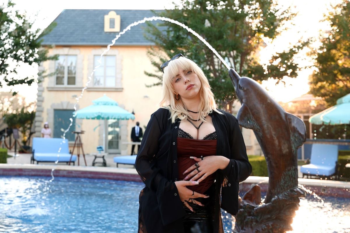 Billie Eilish stands facing the camera with a dolphin fountain in the background.
