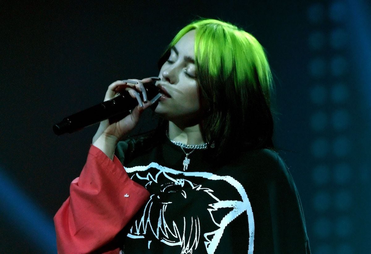 Billie Eilish with green hair sings into a microphone.