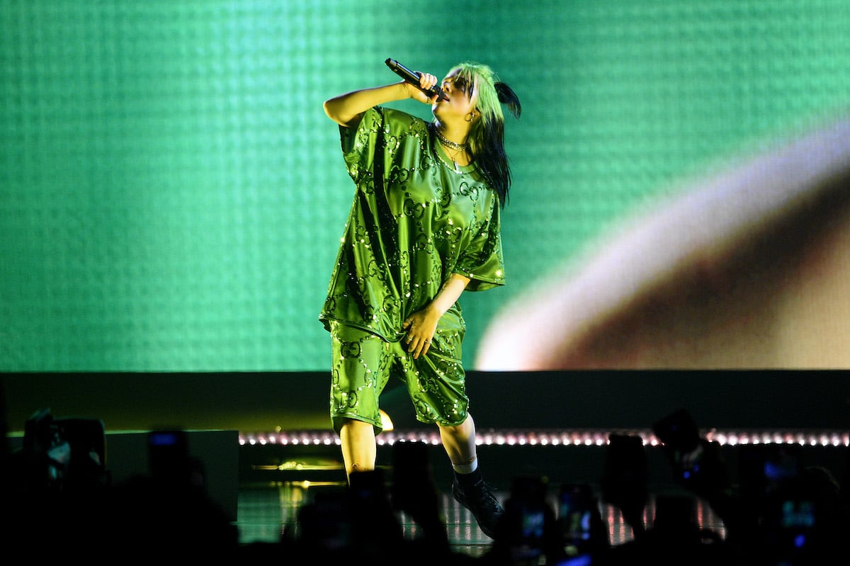 Billie Eilish performs onstage in a bright green outfit with a black and green background.