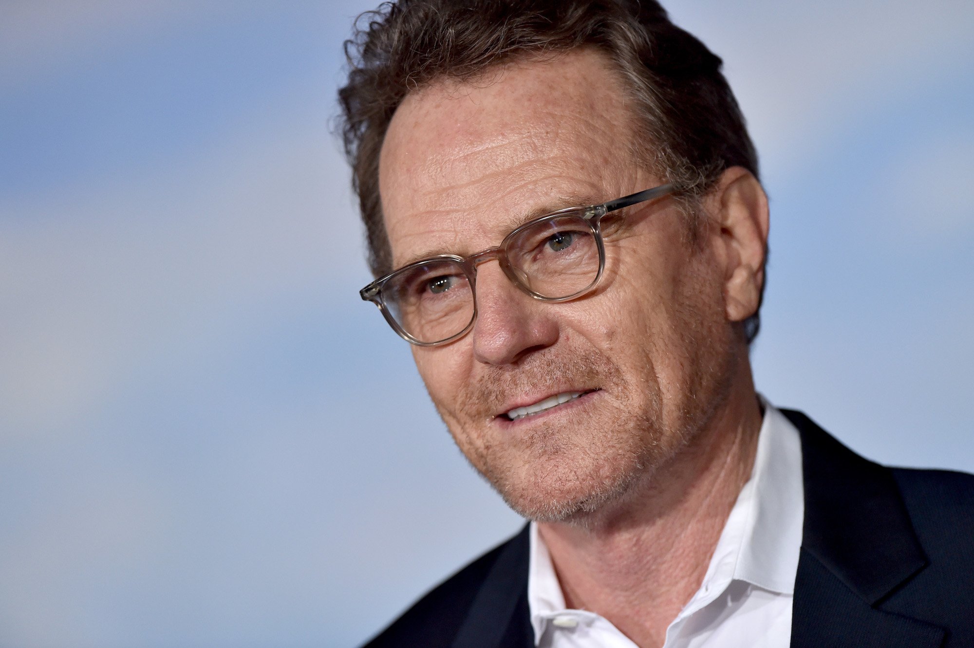 Breaking Bad's Walter White star Bryan Cranston wearing glasses and staring ahead with a blue background behind him