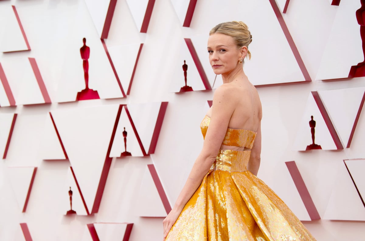 Carey Mulligan looks over her shoulder at the camera, wearing a long strapless gold gown.